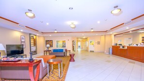 A spacious hotel lobby with a reception desk, seating area, and a television.