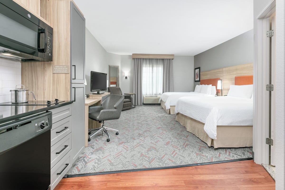 A hotel room with a kitchenette, a bed, a desk, and a television.