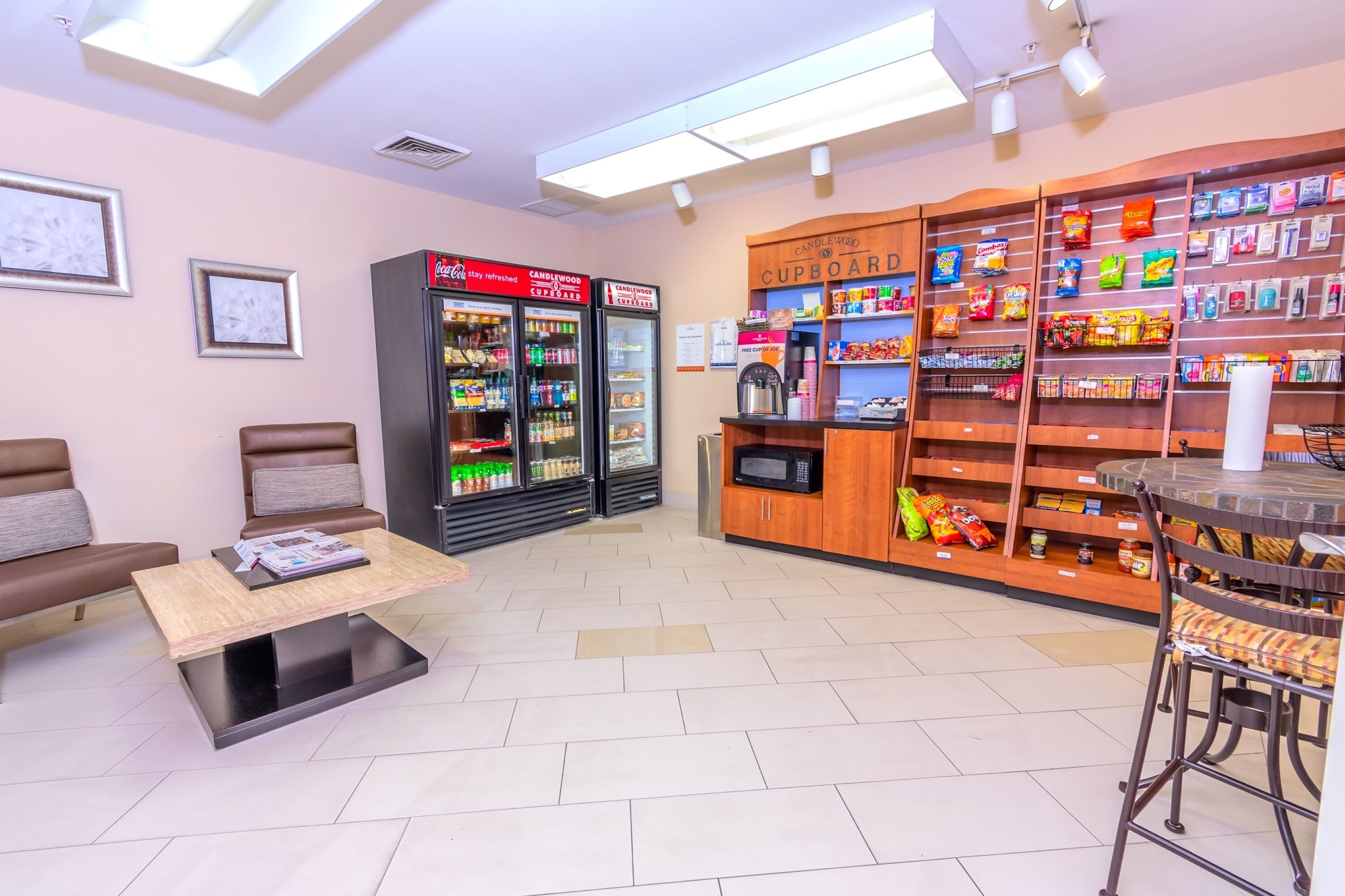 Een gezellig café met zitplaatsen, een koelkast vol drankjes en schappen met snacks.