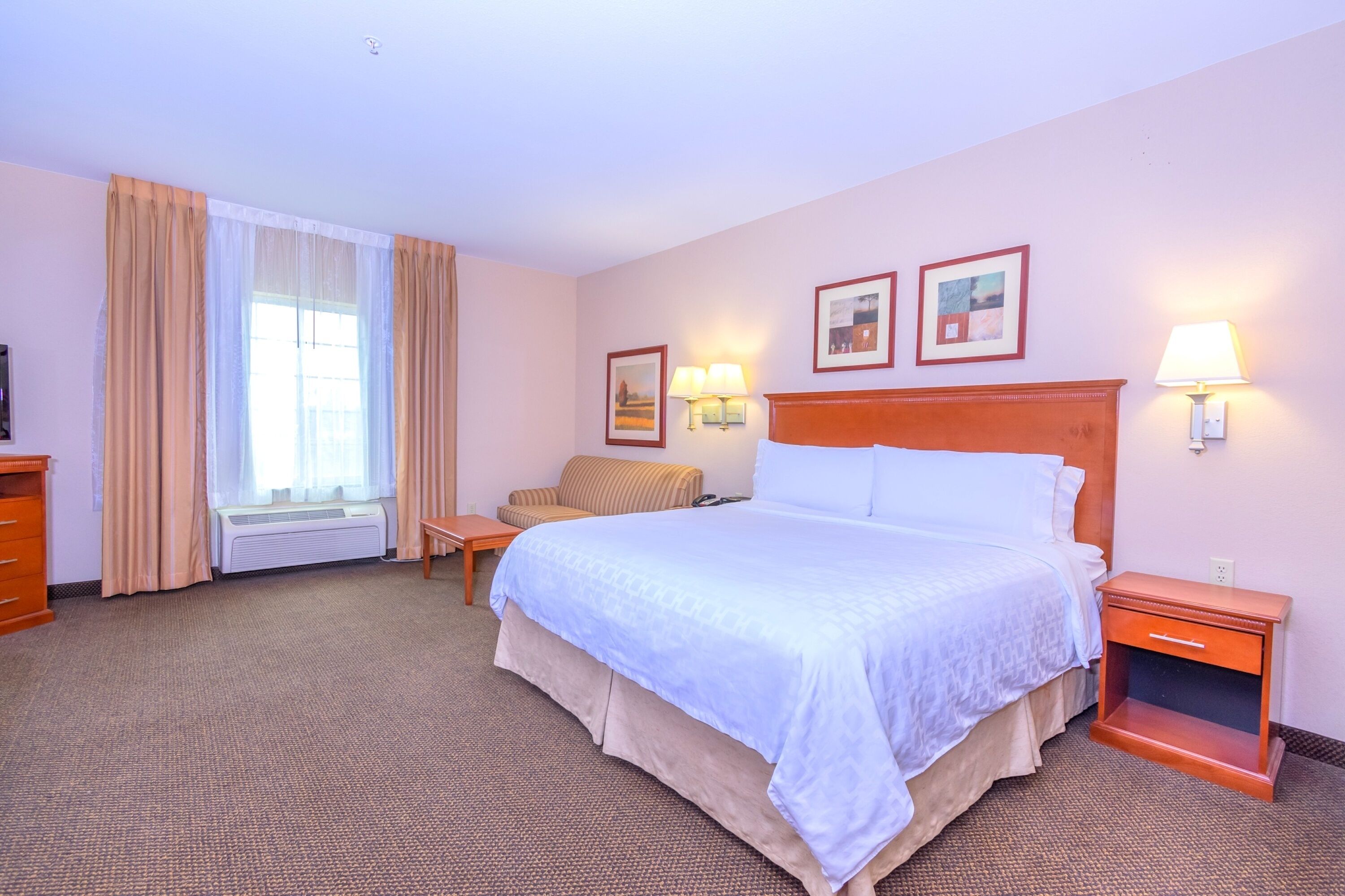 Une chambre d’hôtel avec un grand lit, une table de chevet, une chaise, un bureau et une fenêtre avec des rideaux.