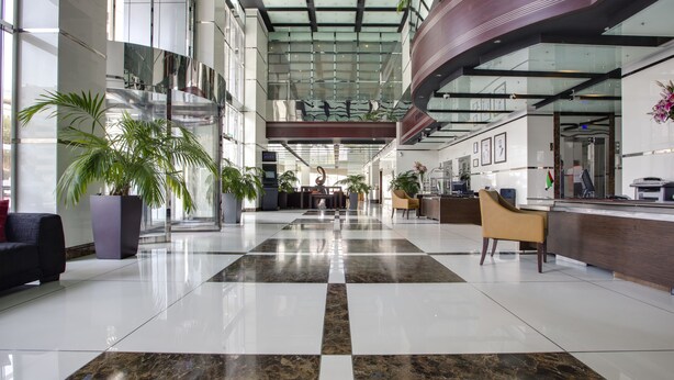 En rymlig entréhall med ett rutmönstrat golv, stora krukväxter och en receptionsdisk.