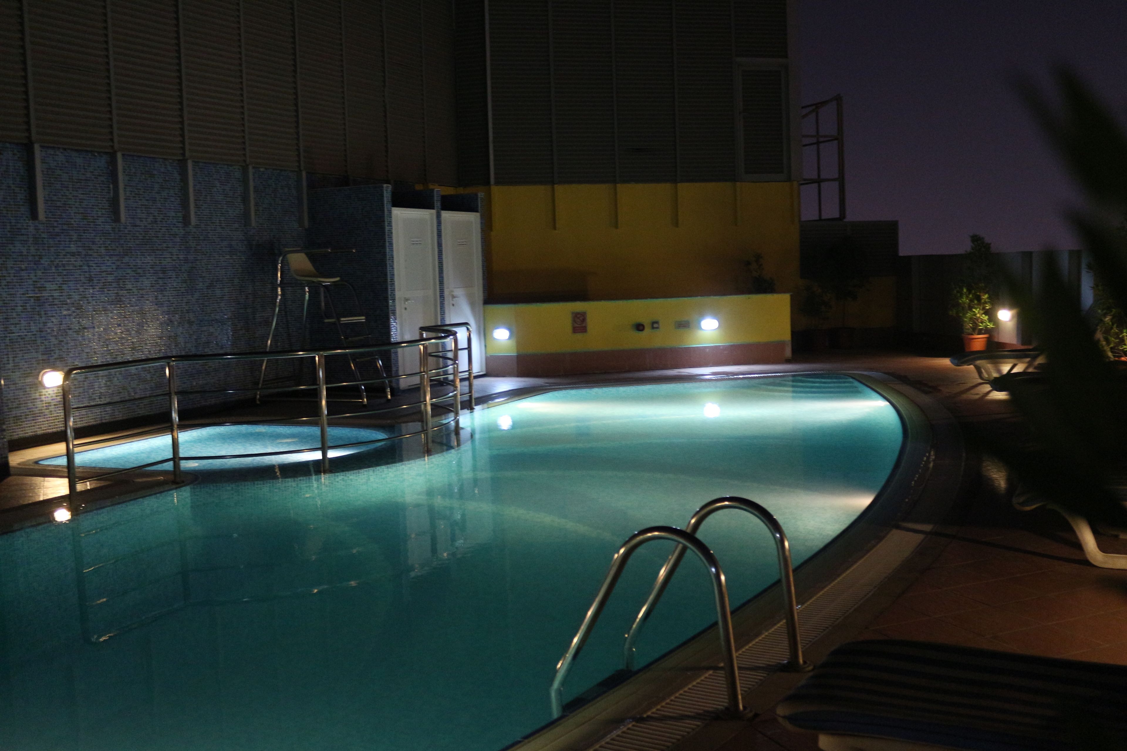 An indoor swimming pool with a tiled wall, a ladder, and a few chairs around the pool.