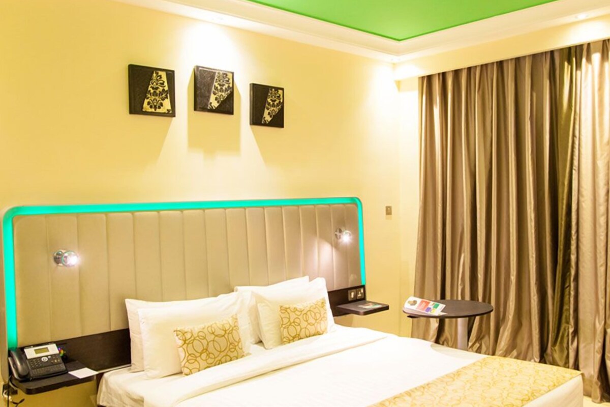 A hotel room with a bed, a nightstand, a phone, and a small table with a menu.