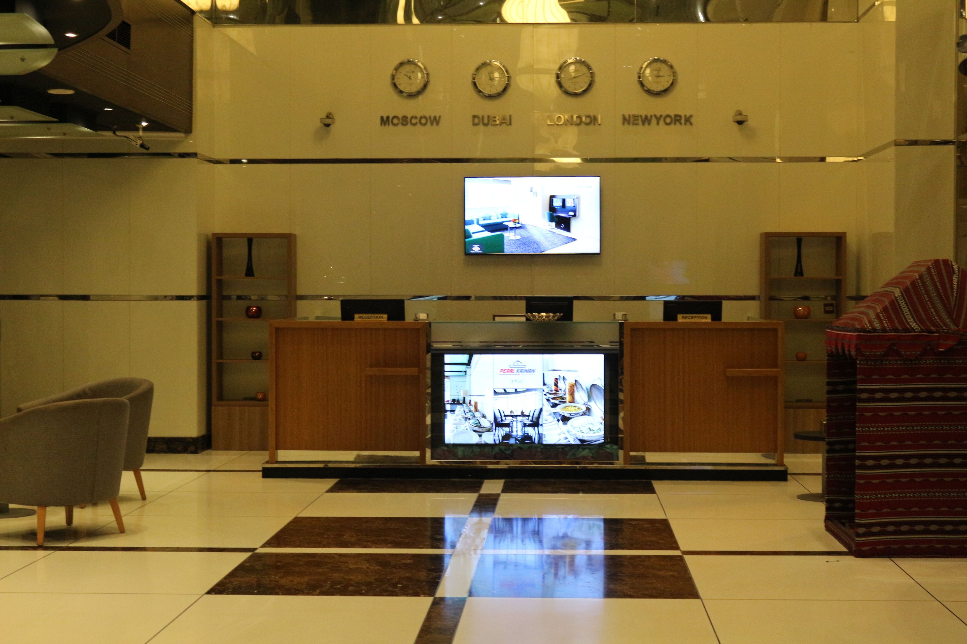 A lobby with a checkered floor, a television displaying a restaurant, and a reception desk.