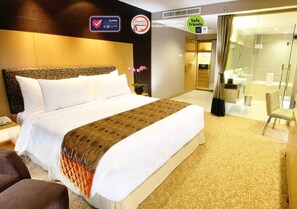 A hotel room with a large bed, a desk, a chair, and a bathroom with a glass shower.