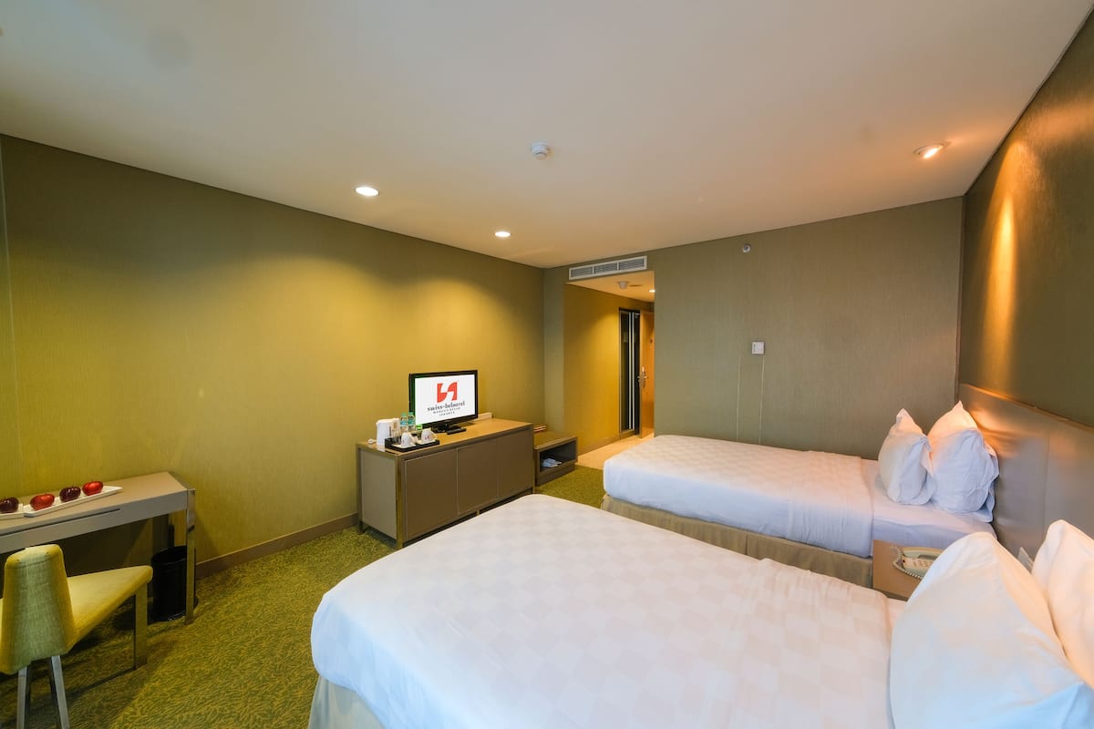Ein Hotelzimmer mit zwei Betten, einem Schreibtisch und einem Fernseher.