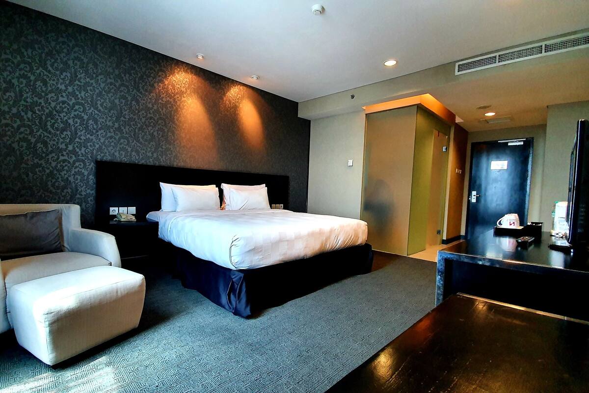 Ein Hotelzimmer mit einem Bett, einem Sessel, einem Schreibtisch und einem Fernseher.