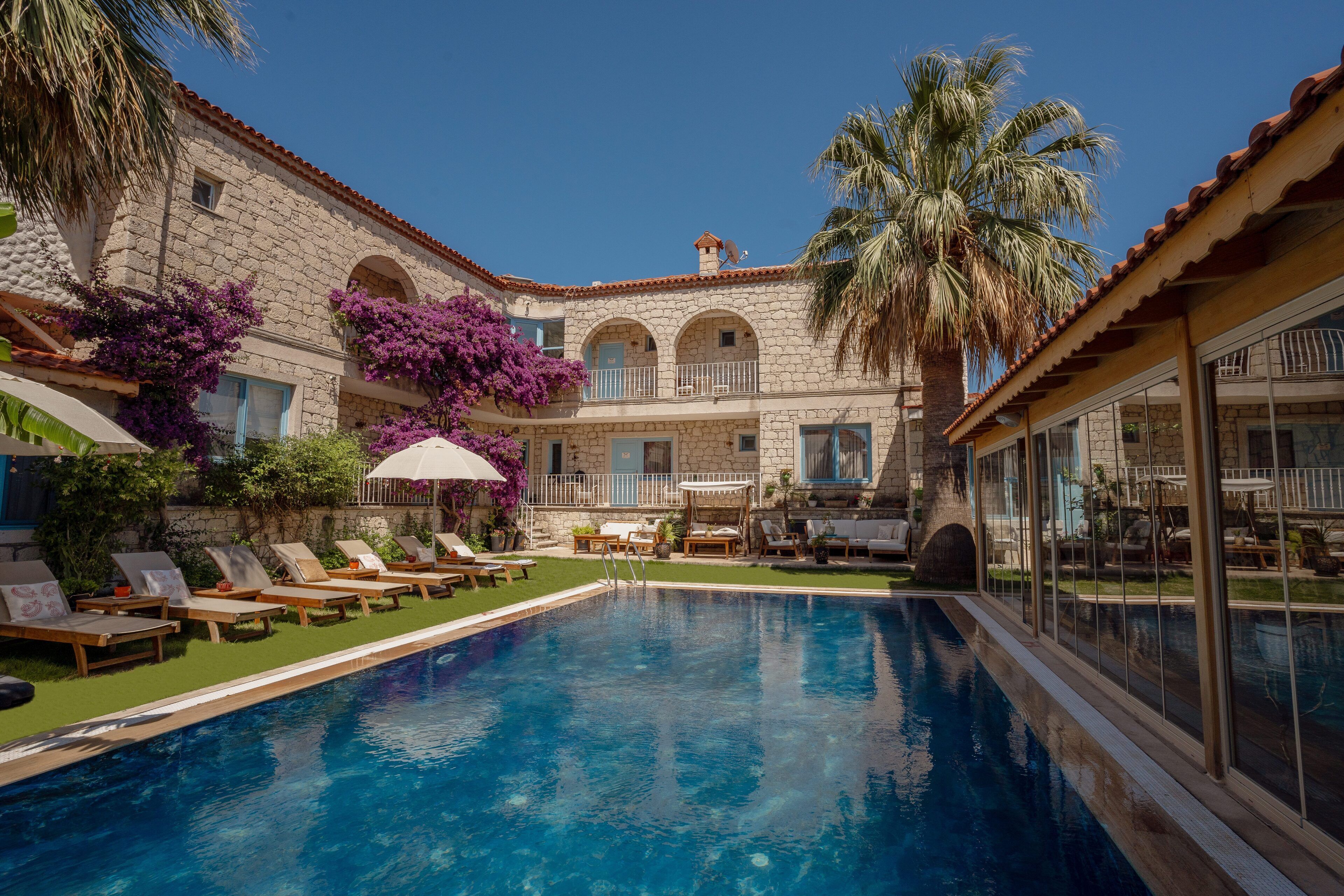 A pool area with lounge chairs, a palm tree, and a stone building with arched windows.