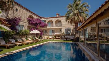 A pool area with lounge chairs, a palm tree, and a stone building with arched windows.