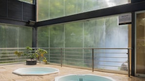 An indoor swimming pool area with two hot tubs, a potted plant, and a sign indicating the location.