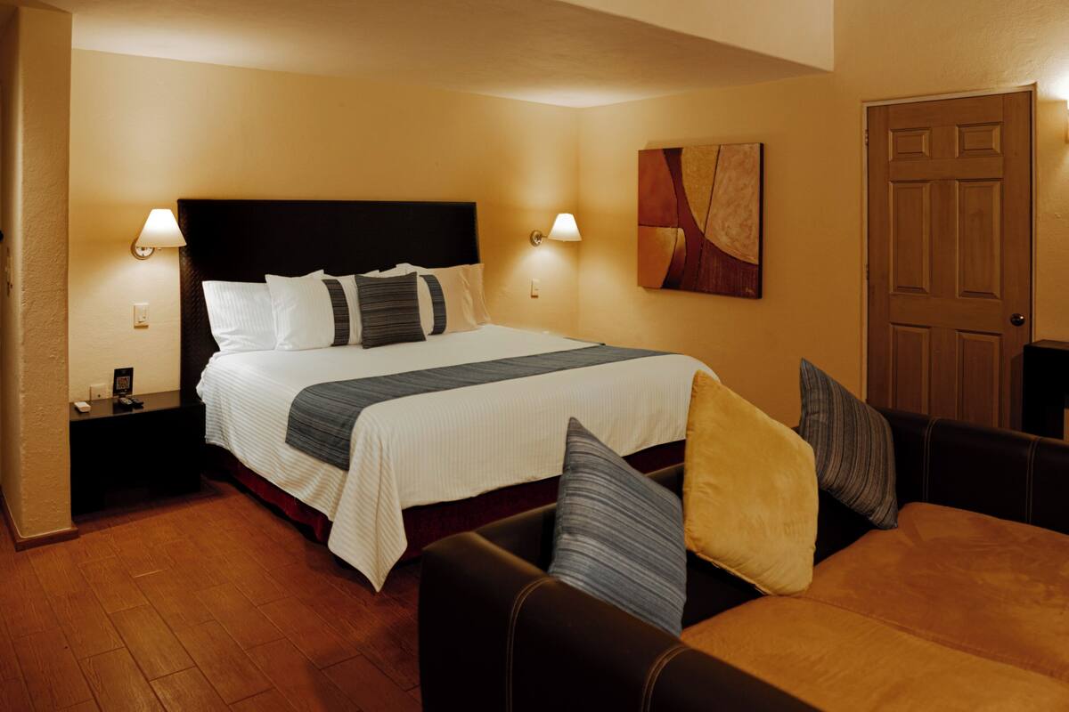 Une chambre d’hôtel avec un grand lit, deux tables de chevet avec des lampes, un canapé et une porte.