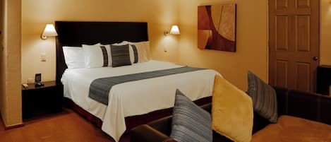 A hotel room with a large bed, two bedside tables with lamps, a sofa, and a door.
