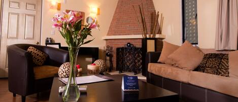 Una sala de estar con chimenea, una mesa de centro con un jarrón de flores y un sofá con cojines estampados.