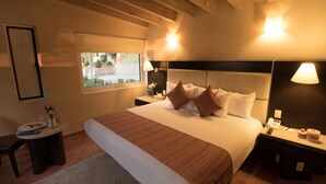 A hotel room with a large bed, a bedside table with a lamp, a nightstand with a phone, and a window with a view of the outdoors.