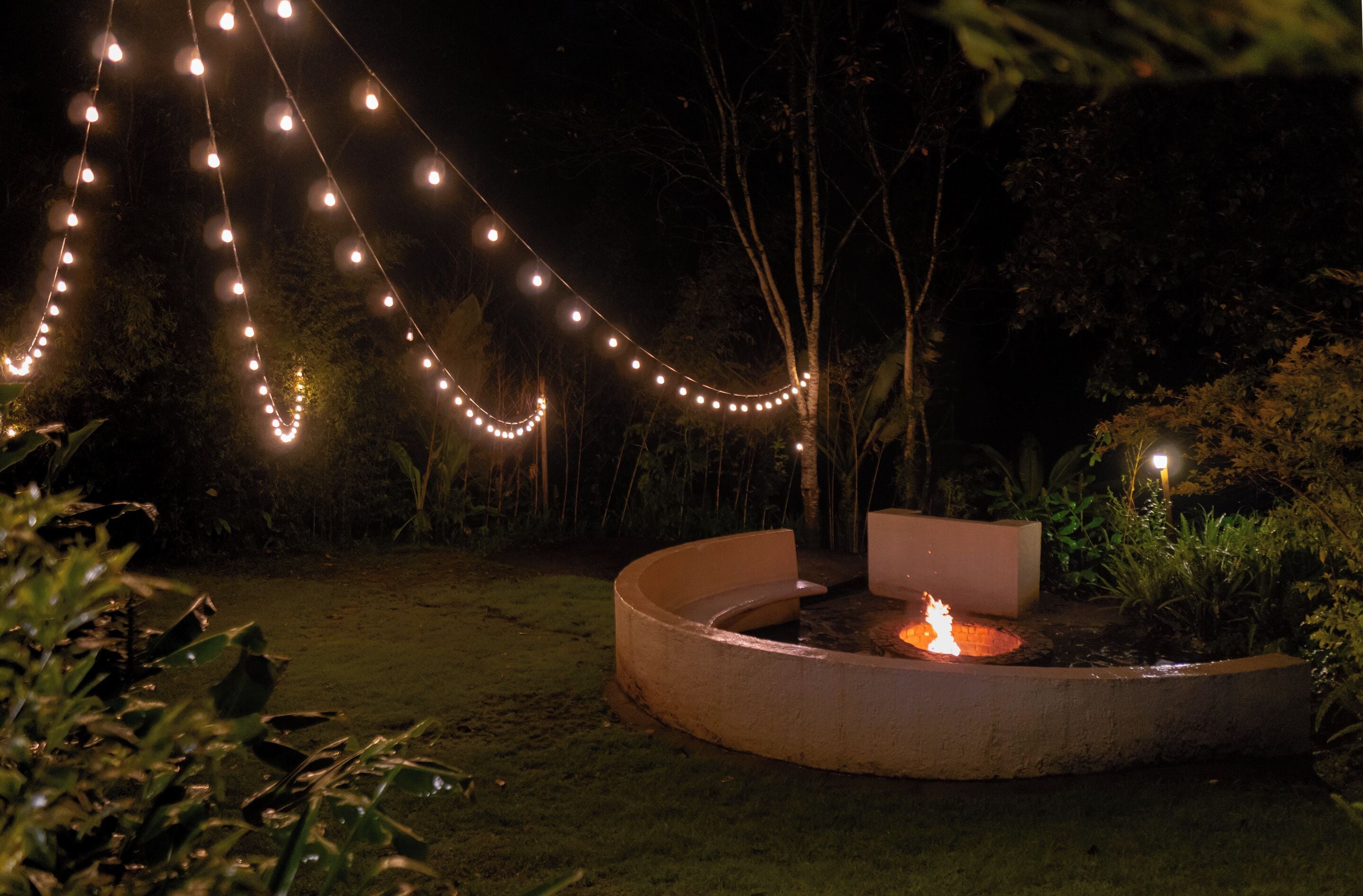 A circular outdoor seating area with a fire pit, surrounded by a low concrete wall and a string of lights.