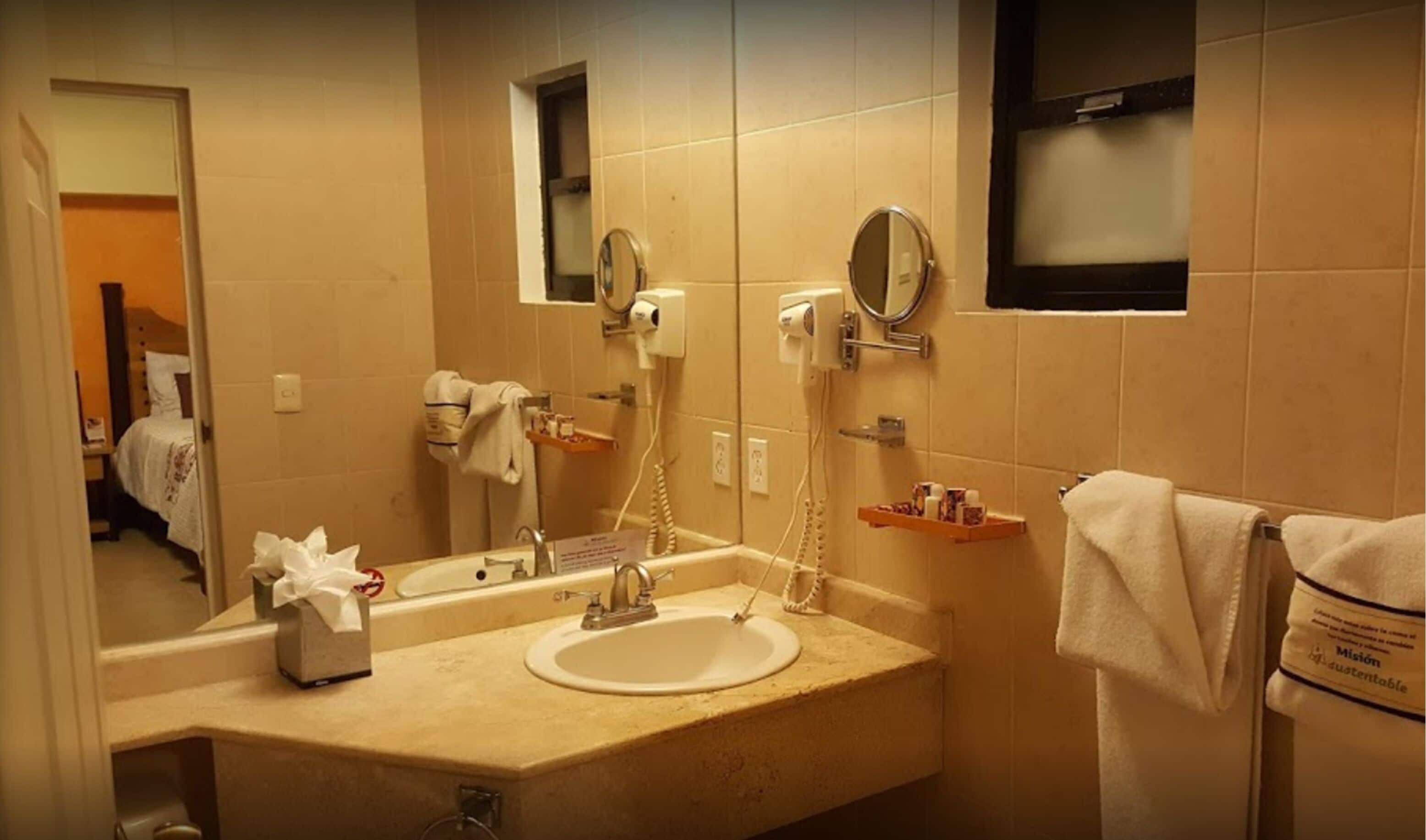 Un baño de hotel con lavamanos, espejo, secador de pelo y toallero.