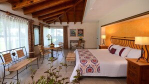 Un dormitorio con una cama grande, vigas de madera en el techo, un escritorio con una silla y una ventana con cortinas.