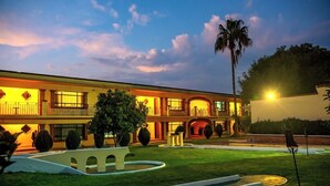 Un edificio de dos pisos con un césped cuidado, una fuente y una palmera.