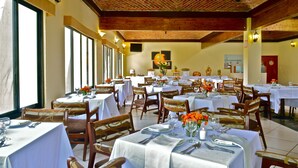 Un restaurante con varias mesas y sillas, dispuesto en un espacio interior amplio con ventanas grandes y techo de ladrillo.