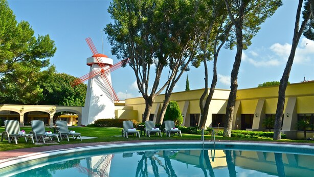 Una piscina con sillones de descanso, un molino de viento y un edificio de fachada amarilla.