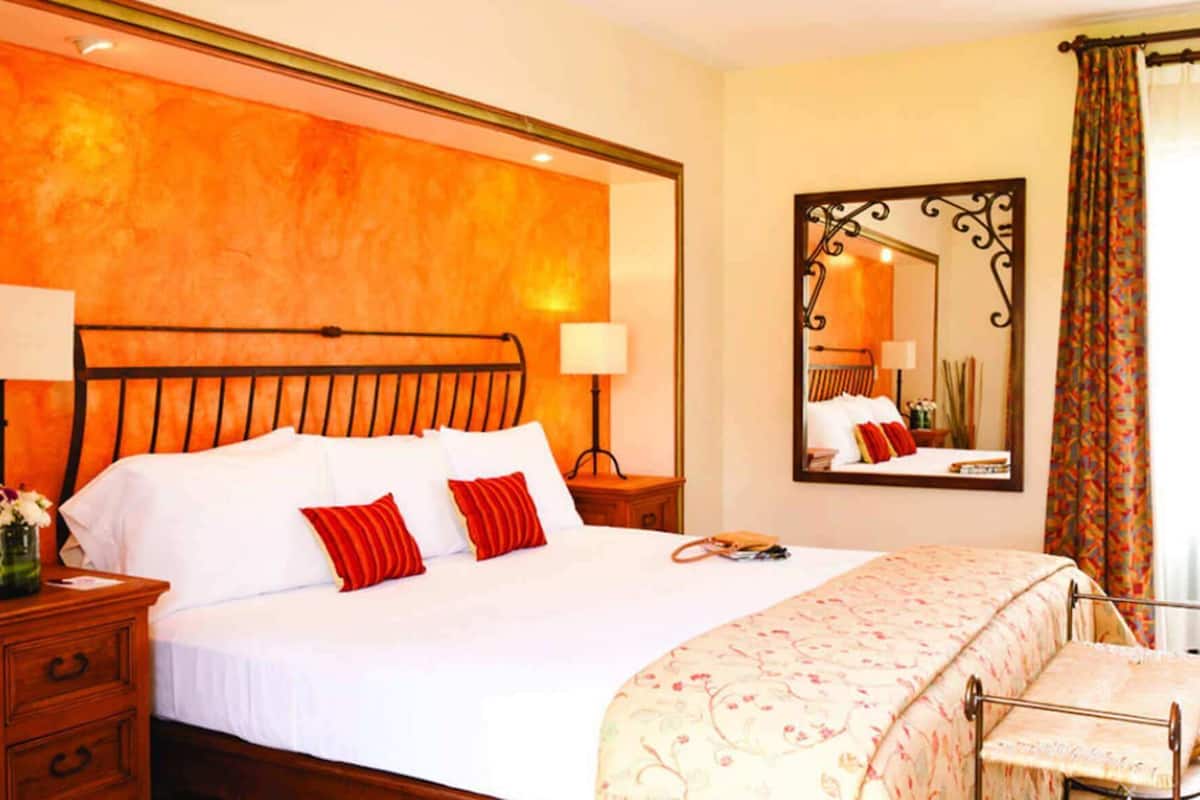 A hotel room with a large bed, a nightstand, a dresser, a mirror, and a window with curtains.