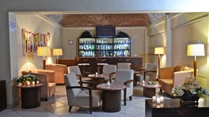 Un vestíbulo de hotel con áreas de estar, un bar con una exhibición de botellas y un televisor montado en la pared.