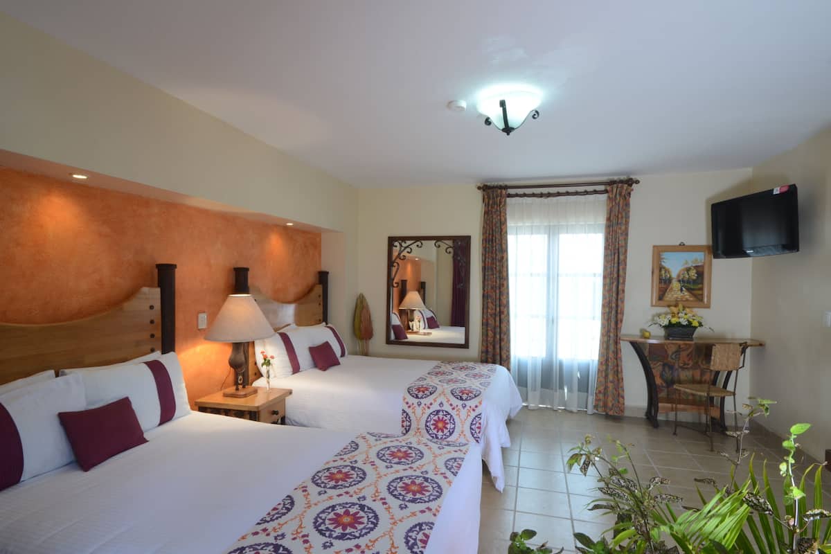 A hotel room with two beds, a desk with a chair, a television, and a window with curtains.