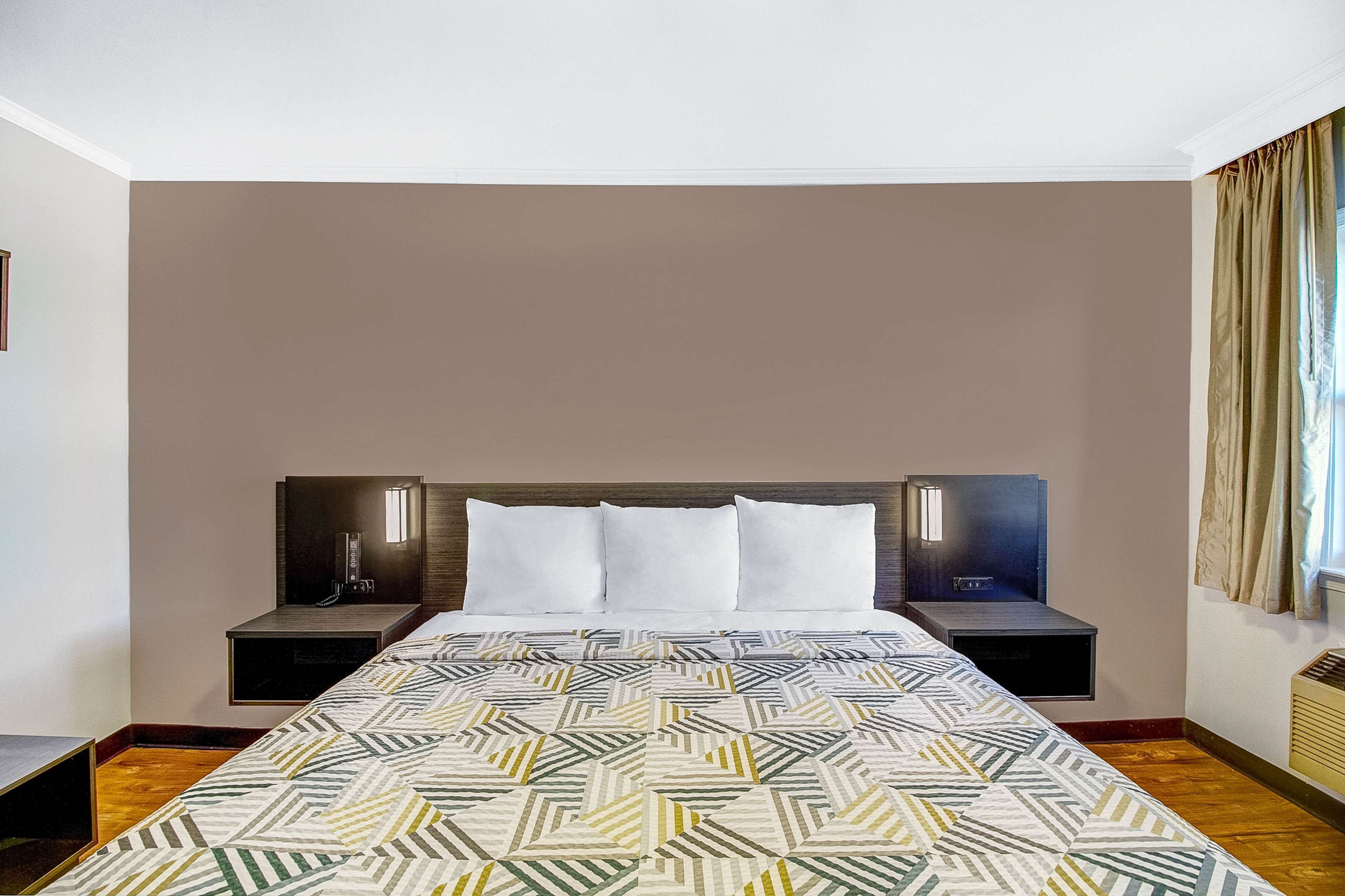 A hotel room with a large bed, two bedside tables, and a headboard with integrated lighting.