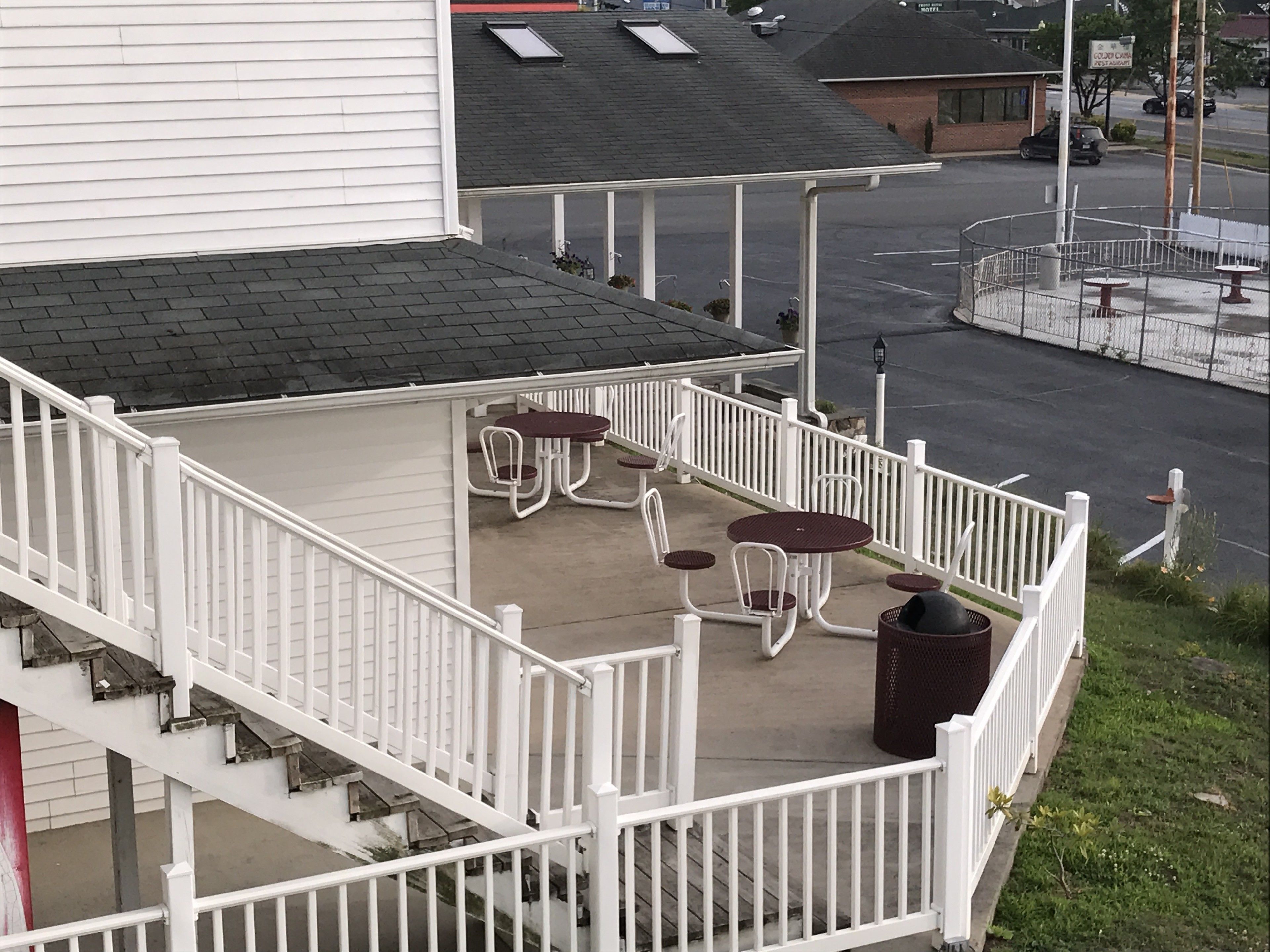 A covered outdoor patio with white railings, a concrete floor, and several tables and chairs.