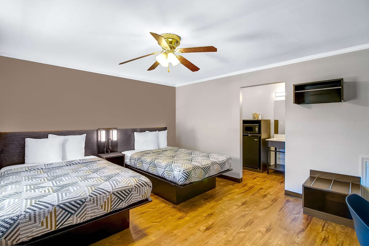 A hotel room with two beds, a ceiling fan, a TV mounted on the wall, and a wooden floor.