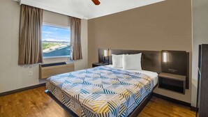 Habitación de hotel con una cama grande, ventilador de techo, mesita de noche, ventana con cortinas y vista al océano.