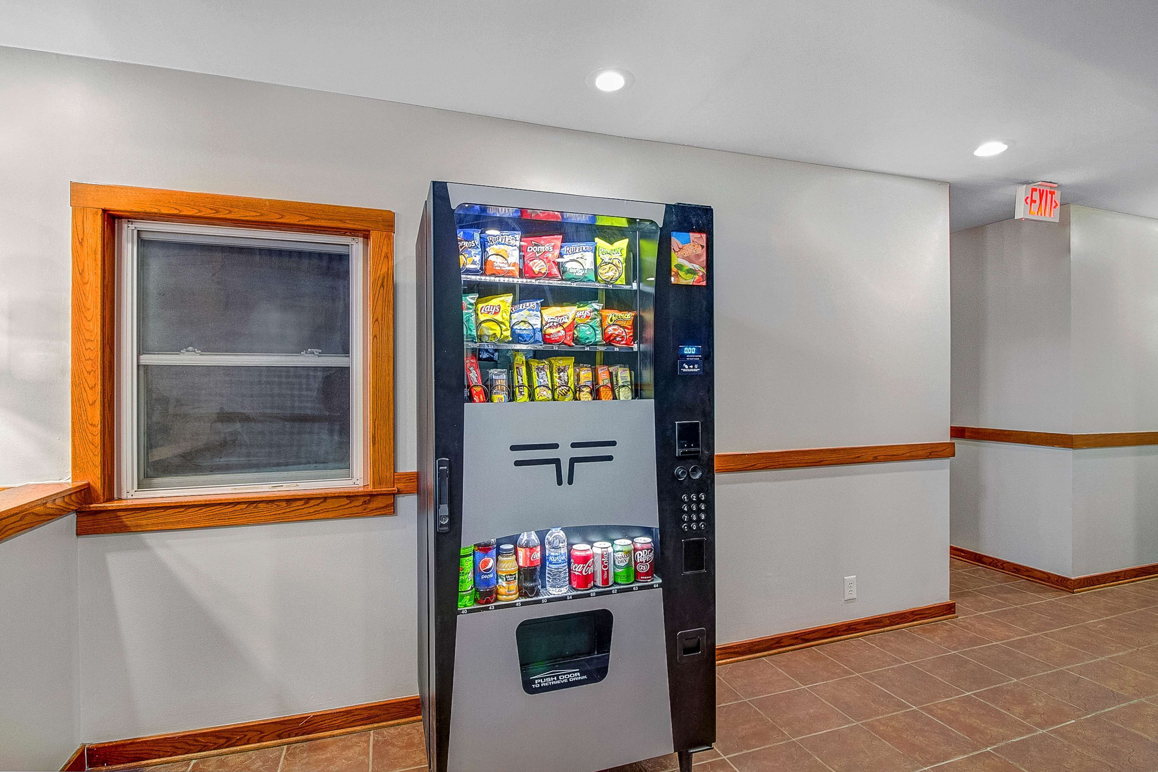 A vending machine with snacks and drinks in a hallway with wooden trim and a window.