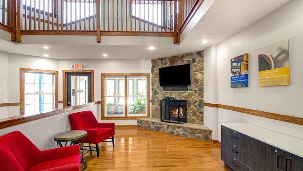 Un hall espacioso con chimenea de piedra, sillones rojos, una escalera de madera y un televisor de pantalla plana montado en la pared.