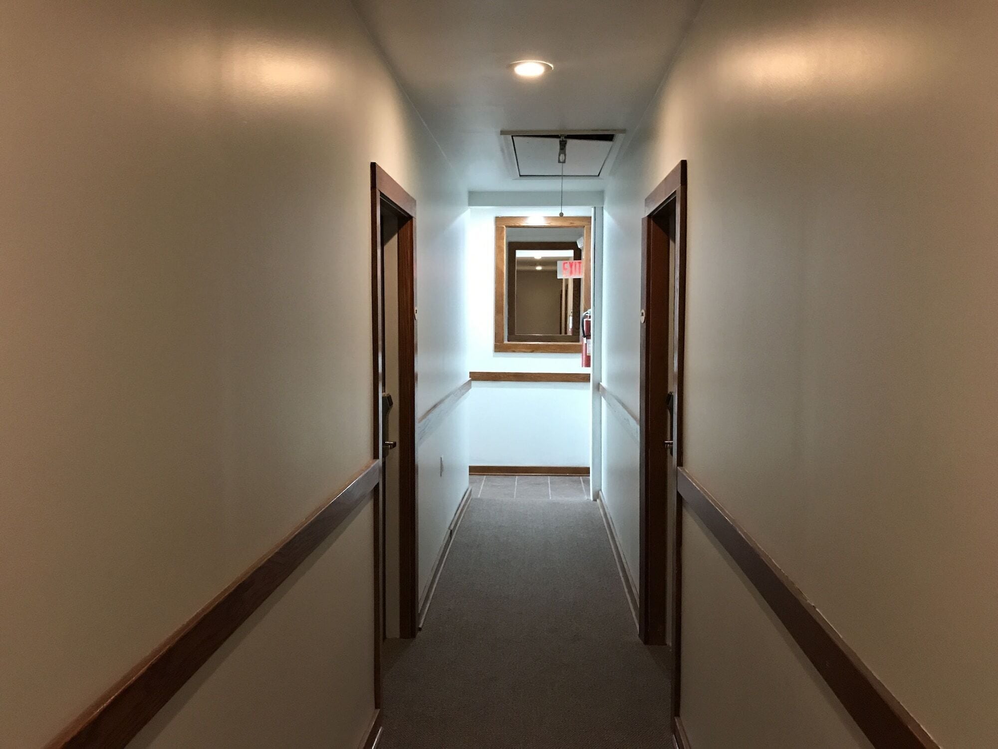 Un couloir étroit, recouvert de moquette, avec des boiseries et un luminaire au plafond.