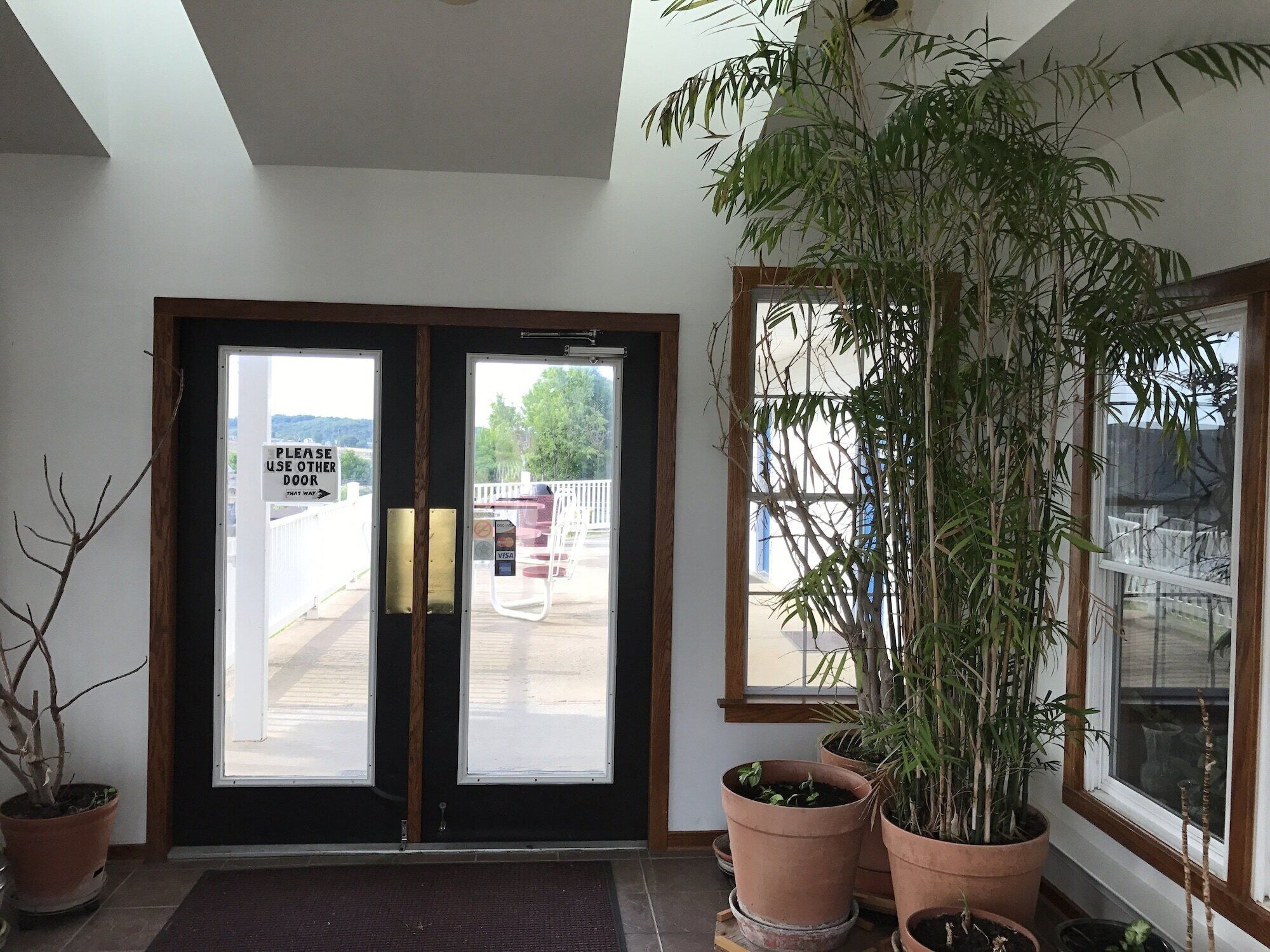 A hotel entrance with a sign directing to use another door, a large potted plant, and a view of the outside.
