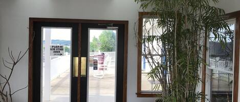A hotel entrance with a sign directing to use another door, a large potted plant, and a view of the outside.