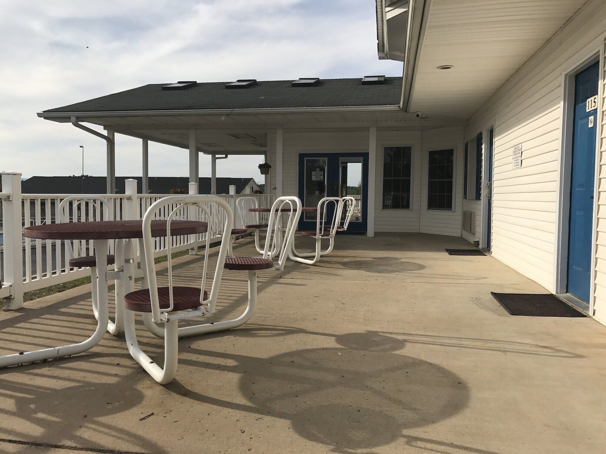 Un espace extérieur aménagé avec des chaises et des tables en métal, une terrasse couverte et un bâtiment doté d’une porte bleue.