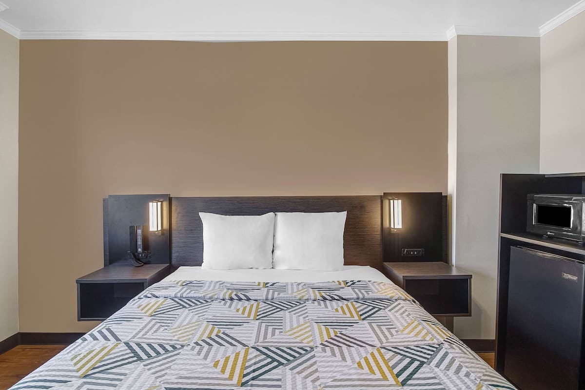 A hotel room with a bed, two bedside tables, a nightstand, a microwave, and a refrigerator.