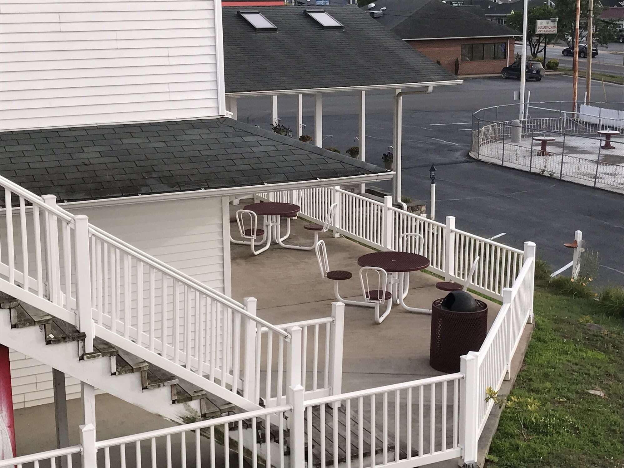 Une terrasse extérieure couverte, dotée de rampes blanches, d’un sol en béton et de plusieurs tables et chaises rondes.