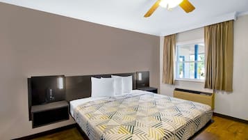 A hotel room with a bed, bedside tables, a ceiling fan, a window with curtains, and a built-in heater.