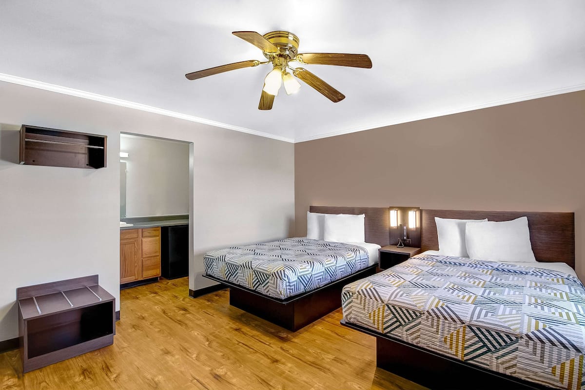 A hotel room with two beds, a ceiling fan, a mirror, and a small cabinet.