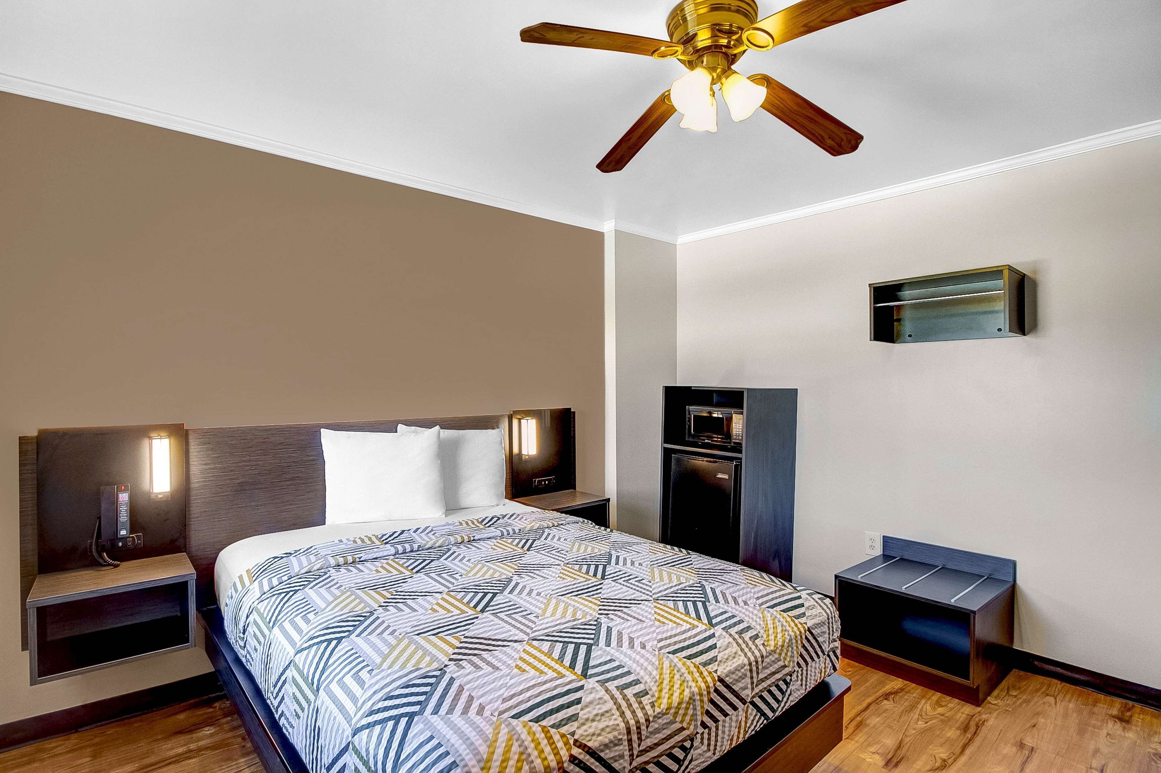 A hotel room with a bed, nightstands, a ceiling fan, a built-in TV, and a microwave.