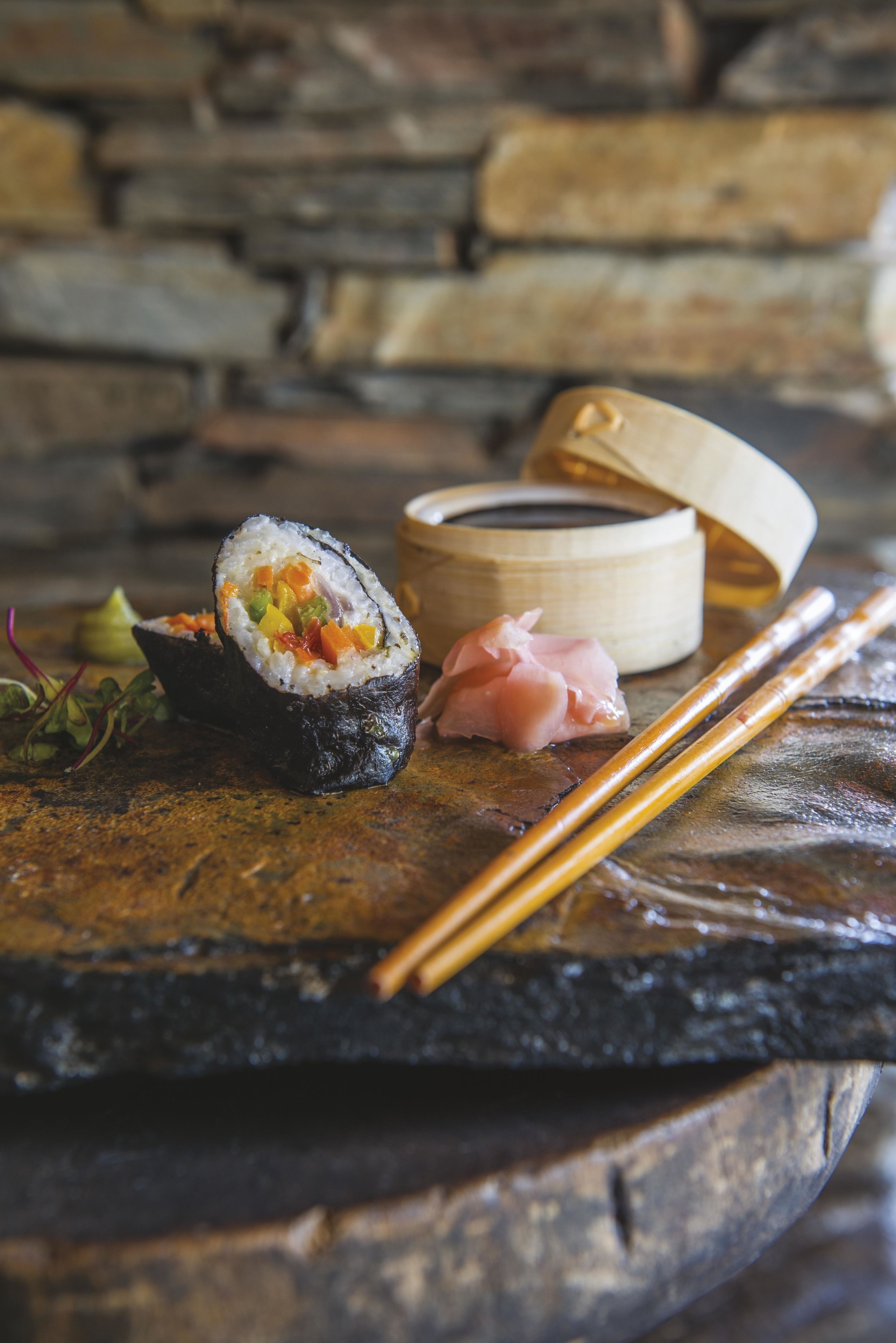 Des sushis servis sur une table en pierre, accompagnés de baguettes et d’un récipient en bois.