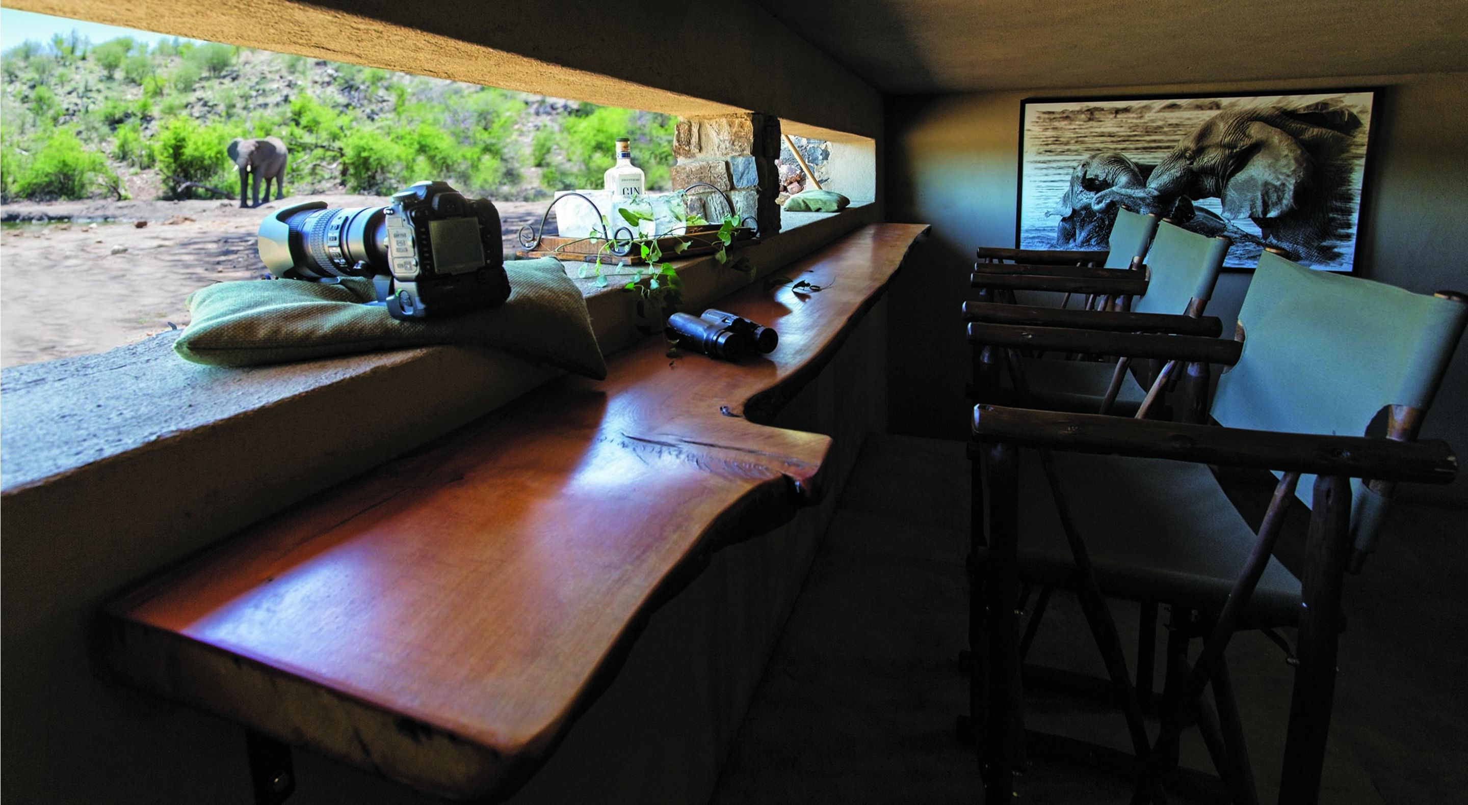 A wooden bench with binoculars, a camera, and a bottle of gin.