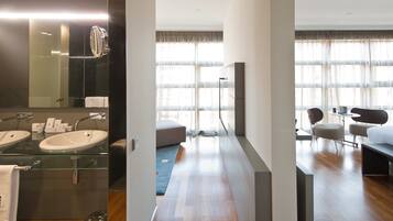 A modern hotel room with a large mirror, two sinks, a sofa, and a dining area.
