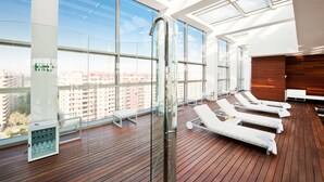 Un moderno salón en la azotea con amplias ventanas, suelo de madera y tumbonas.