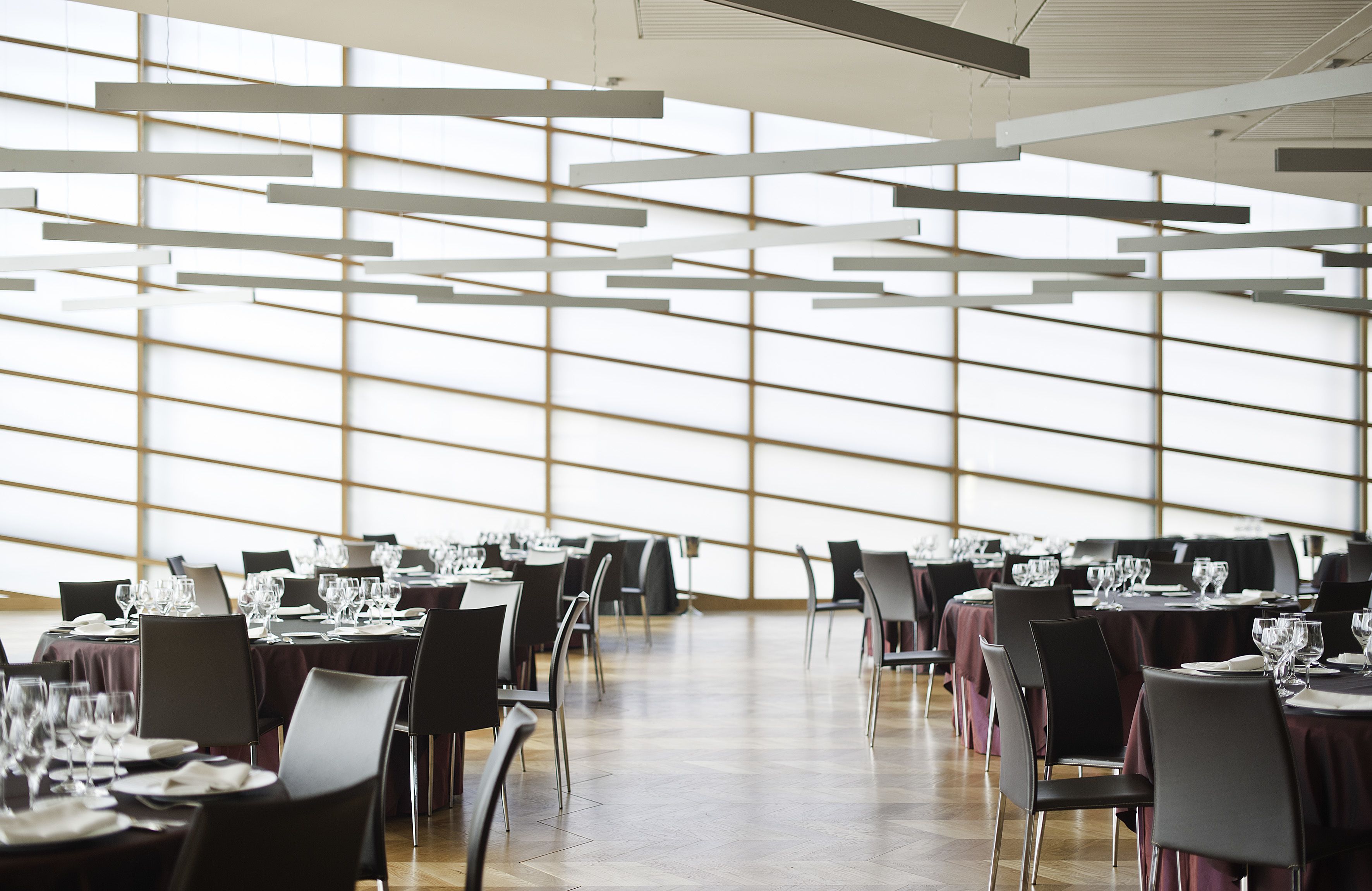 Un vaste espace dédié à la salle à manger, avec des tables dressées pour le repas, de grandes fenêtres et un design moderne au niveau du plafond.