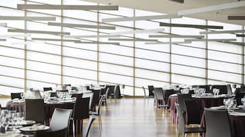 Un vaste espace dédié à la salle à manger, avec des tables dressées pour le repas, de grandes fenêtres et un design moderne au niveau du plafond.