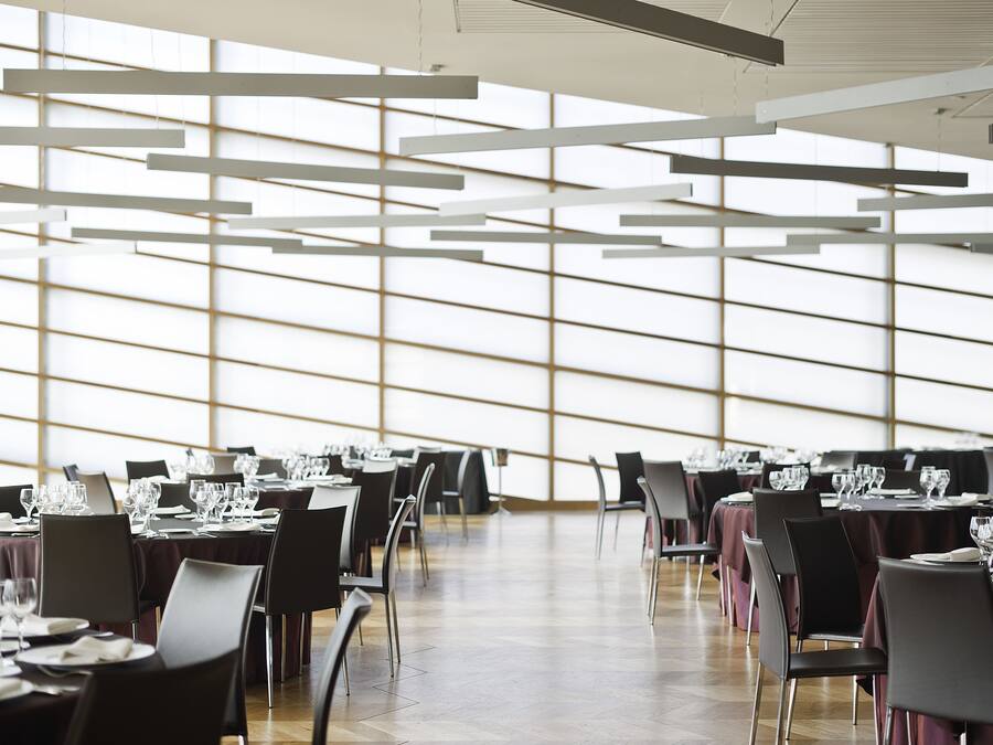Un vaste espace dédié à la salle à manger, avec des tables dressées pour le repas, de grandes fenêtres et un design moderne au niveau du plafond.