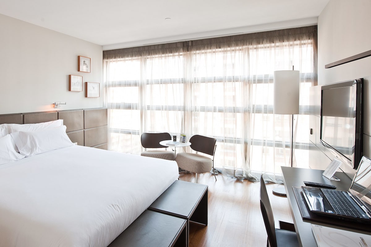 Habitación de hotel con una cama grande, un escritorio con una computadora portátil, una silla y un televisor.